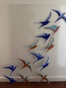 Placa de acrílico con aves pintadas en tonos azul, turquesa y cobre en vuelo - detalle del frontal de la obra "Las aves deben vivir libres"